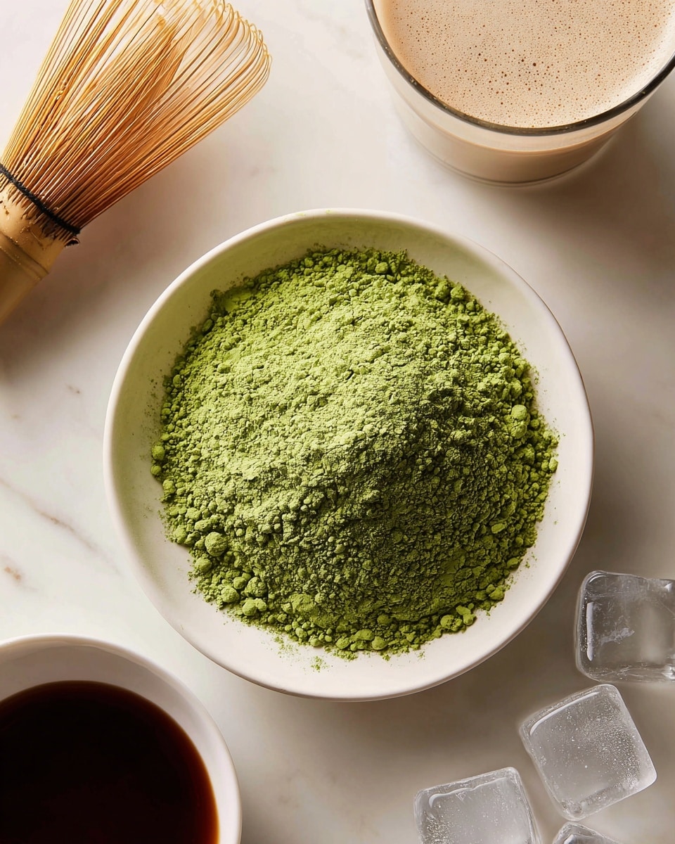 A close-up view of a small white bowl filled with a heap of bright green matcha powder with a fine, slightly clumped texture in the center. To the left of the bowl is a bamboo whisk with thin, evenly spread prongs. At the top right corner, there is a glass of light creamy beige liquid with small frothy bubbles on the surface. At the bottom left corner is a small white bowl filled with dark liquid, and at the bottom right are several clear ice cubes on a white marbled surface. photo taken with an iphone --ar 4:5 --v 7