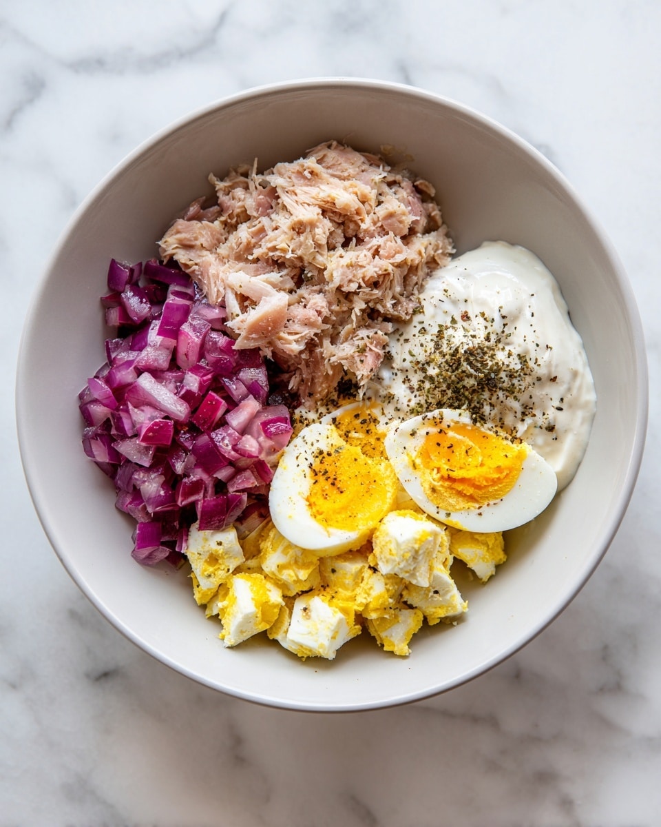 A white plate with white marbled texture holds a single slice of toasted brown whole wheat bread, roughly cut at the edges. On top of the toast is a thick, uneven layer of a chunky mixture made of small pieces of white and orange egg bits, light pinkish shredded tuna, and tiny bits of purple onion. The mixture looks creamy with specks of black pepper scattered on top and around the plate. Photo taken with an iphone --ar 4:5 --v 7