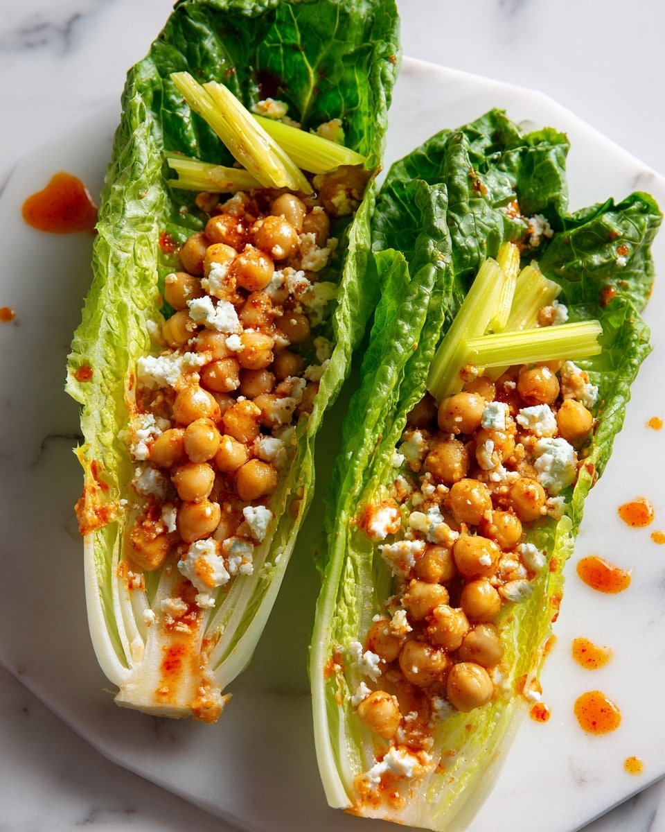 Two fresh green romaine lettuce leaves lie side by side on a white marbled surface, each serving as a boat filled with a mixture of light brown chickpeas, small orange carrot pieces, and tiny white cheese crumbs. The lettuce leaves show a gradient from dark green outer edges to lighter green and almost white near the center. A few small yellow celery leaf pieces rest on top of the filling. The dish has a slight drizzle of reddish-orange sauce scattered over the chickpea mixture, adding a touch of color contrast photo taken with an iphone --ar 4:5 --v 7