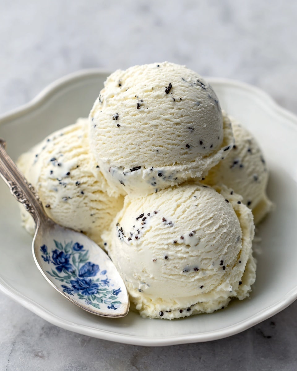 Three scoops of pale creamy white ice cream sit close together in the center of a shallow white bowl with a smooth matte finish. The texture of the ice cream looks soft and slightly melting, with small creases and swirls on the surface. Behind the scoops, a shiny golden spoon rests inside the bowl. The bowl is placed on a white marbled surface, and in the blurred background, there is a colorful fabric with a floral pattern featuring pink, orange, green, and purple hues. The image has a bright, natural light feel. photo taken with an iphone --ar 4:5 --v 7