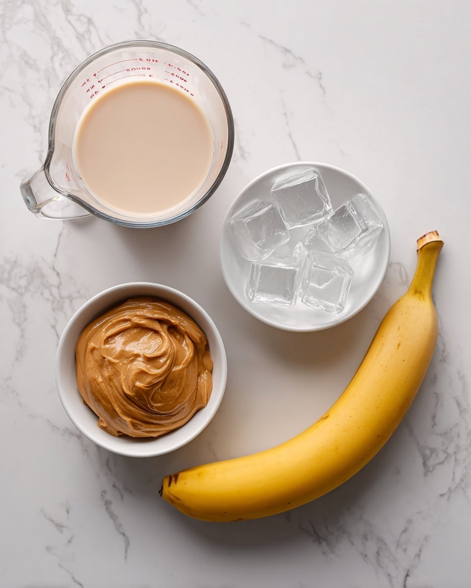 The image shows four ingredients on a white marbled surface. In the top left, there is a glass measuring cup filled with light beige almond milk. To the right of it, there is a white bowl filled with several translucent ice cubes. Below the measuring cup, there is a small white bowl with creamy, brown almond butter inside. At the bottom right corner, there is a whole yellow banana laying horizontally with a slight curve. Each ingredient is labeled with simple black text on white rectangles placed on or near them. Photo taken with an iphone --ar 4:5 --v 7