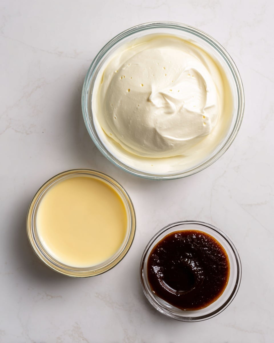 A top-down view shows three clear glass bowls on a white marbled surface. The largest bowl, centered at the top, holds smooth, white heavy whipping cream with a slightly bubbly surface. Below it to the left is a medium bowl filled with pale yellow sweetened condensed milk, its surface smooth and glossy. To the right of this is a small bowl containing dark brown vanilla bean paste with a rich, thick texture. Each bowl is clean and clear, highlighting the contrasting colors and textures of the ingredients. Photo taken with an iphone --ar 4:5 --v 7
