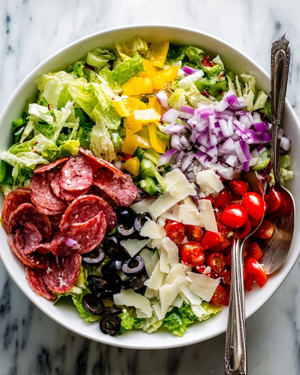 A large white bowl filled with a colorful Italian salad made of many chopped layers including bright green lettuce pieces as the base, scattered with thin slices of reddish-pink salami, black olive slices, small bright yellow pepper rings, and halved red cherry tomatoes. There are also white shavings of cheese and pale pieces of celery mixed throughout, along with finely chopped red onion to add a pop of purple. Two vintage silver spoons rest in the bowl, partially buried in the fresh salad. The bowl is set on a white marbled surface photo taken with an iphone --ar 4:5 --v 7