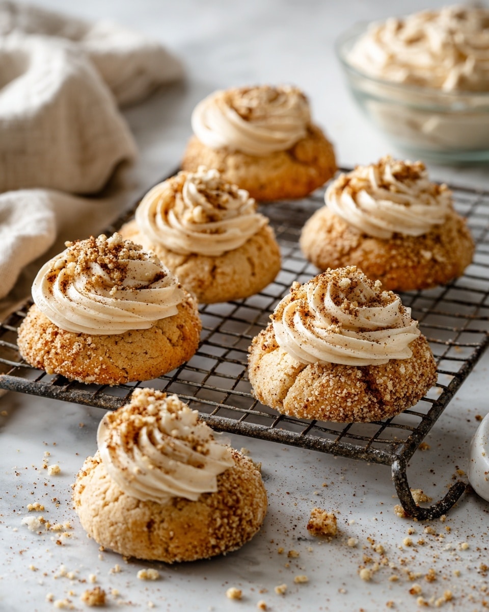 The image shows six small round cakes with a crumbly light brown base topped with a swirl of beige cream that has a smooth and fluffy texture. Each cake is sprinkled with fine brown crumbs on the cream, adding a slightly rough texture. The cakes are arranged on a white marble surface, with four placed directly on the surface and two on a metal cooling rack. To the right, there is a clear glass bowl with more of the brown crumbs inside. Small crumbs are scattered around the cakes and bowl on the marble. The overall look is warm and cozy with soft natural light. Photo taken with an iphone --ar 4:5 --v 7