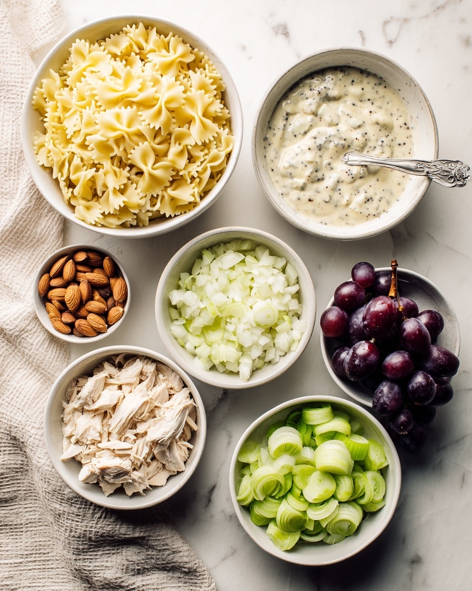 The image shows six white bowls arranged on a white marbled surface, each containing a different ingredient for a pasta salad. The largest bowl at the top left holds yellow bow-tie pasta with a rough texture. To its right is a bowl with creamy white poppyseed dressing speckled with tiny black seeds and a spoon inside. Below the dressing, a smaller bowl is filled with roughly chopped white onion pieces. To the left of the onion bowl is a bowl with shredded light beige chicken. At the center bottom, a bowl contains chopped bright green celery. Next to it, on the bottom left, is a bowl of whole brown almonds. To the right of the celery bowl, a bowl is filled with dark purple grapes, some sliced in half showing green insides. A beige textured cloth is partially visible at the left edge. The light in the image is soft, and the composition is neat and clear. photo taken with an iphone --ar 4:5 --v 7