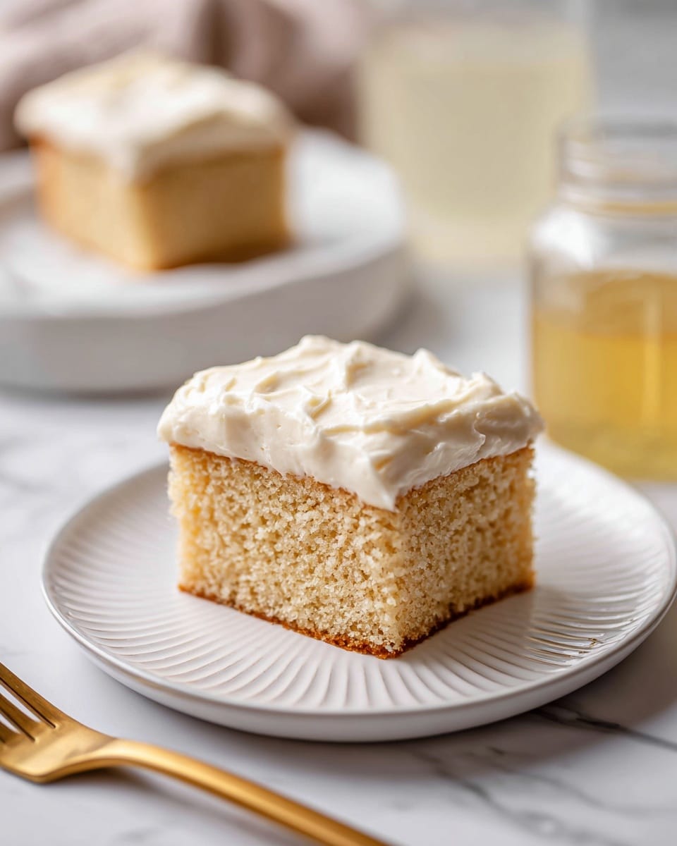Three square pieces of light brown cake are stacked on top of each other on a white marbled surface. The cake has a soft and moist texture with small holes inside. The top piece is dusted lightly with powdered sugar, adding a delicate white layer on top. In the background, there is a clear glass container with a creamy yellow spread and two white sticks inside it, slightly blurred. The image has soft natural lighting, highlighting the texture of the cake. Photo taken with an iphone --ar 4:5 --v 7