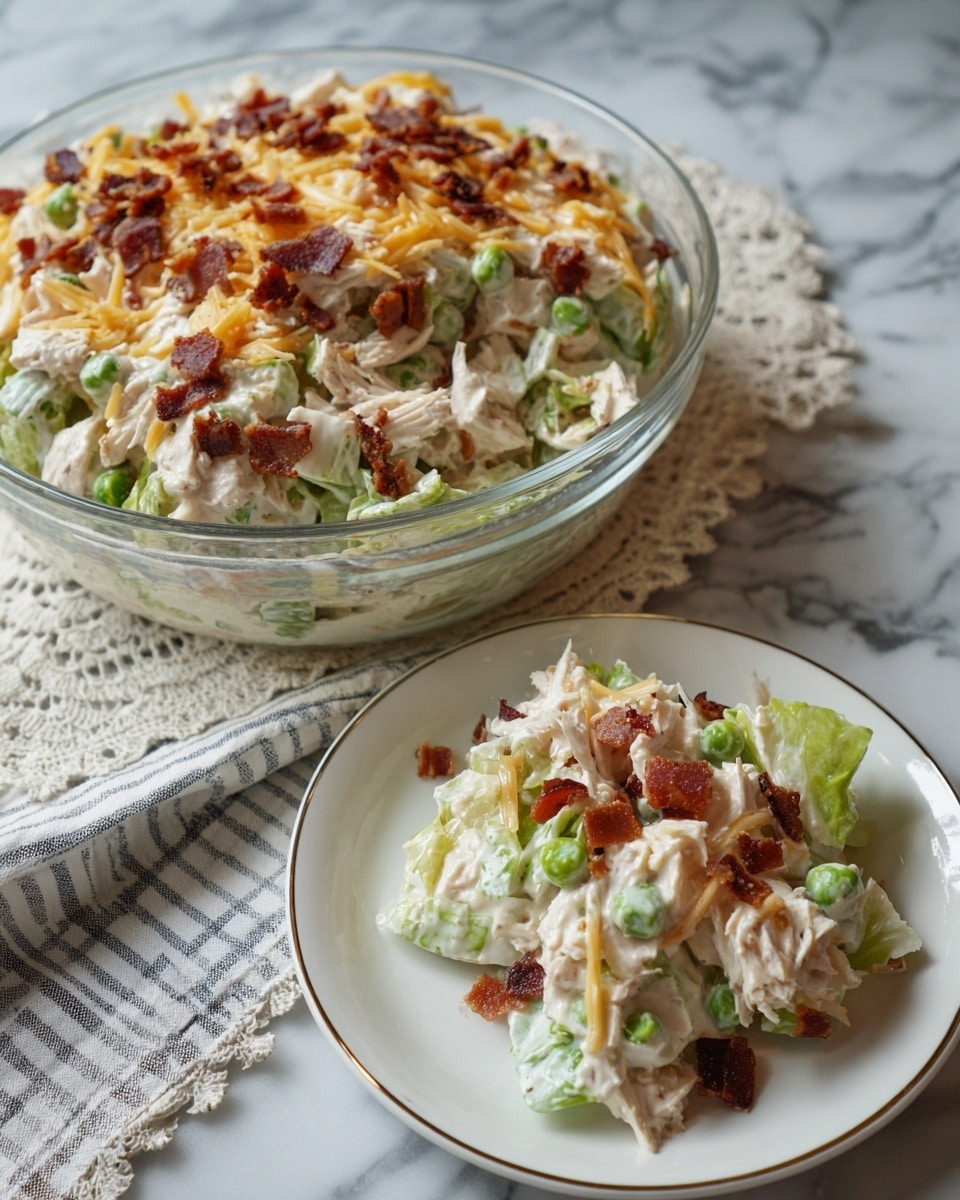 A layered salad is shown in a large clear glass bowl on a white marbled surface. The top layer is covered with light yellow shredded cheese, sprinkled with small brown crispy bacon bits. Underneath, a white creamy layer is visible, and below that a layer of green lettuce leaves can be seen through the bowl. In front of the bowl, there is a smaller white plate with an embossed flower pattern holding a lifted portion of the salad. The salad on the plate shows green leafy lettuce mixed with creamy dressing, bacon bits, and shredded cheese on top. The scene includes a lace cloth and green-striped cloth beneath the bowl and plate. Photo taken with an iphone --ar 4:5 --v 7