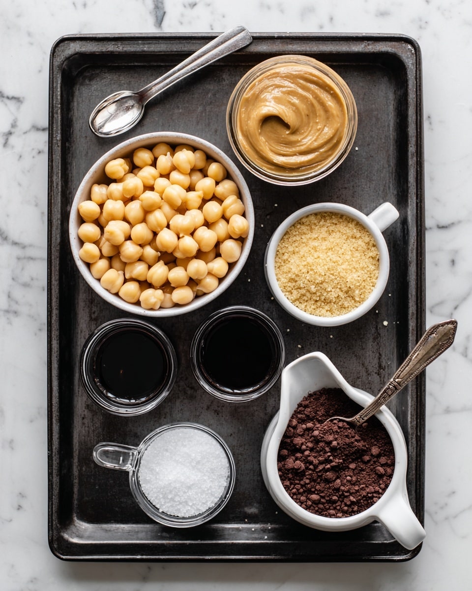 A top-down view of a dark baking tray on a white marbled surface, holding several small containers with ingredients. On the left side, a white bowl is filled with round pale yellow chickpeas, next to a small glass container of light brown nut butter with a smooth texture. Below these, a small clear glass has dark vanilla liquid. On the right side of the tray, a small white cup contains light golden brown sugar with a crumbly texture, next to a small white pitcher filled with dark maple syrup. Below the sugar, a metal spoon holds a small heap of white salt, and beside it a measuring spoon is heaped with dark brown cocoa powder. The arrangement is neatly spaced and labeled. Photo taken with an iphone --ar 4:5 --v 7
