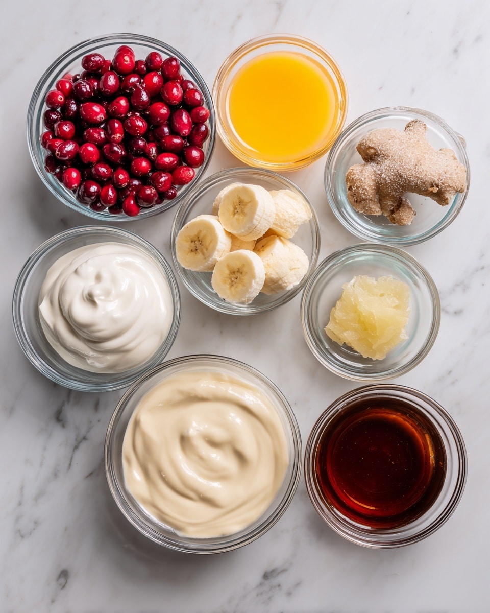 The image shows eight clear glass bowls arranged on a white marbled surface, each containing a different ingredient. Starting from the top left, the first bowl has bright red cranberries, the next bowl to the right holds orange juice with a vibrant yellow color. Below the cranberries is a bowl with two frozen banana halves covered lightly with frost. To the right of the bananas is a bowl filled with creamy non-dairy milk in a light beige color. Moving downwards, a bowl on the left contains smooth unsweetened yogurt with soft peaks and a white tone. To its right, there is a small bowl with dark amber maple syrup, followed by a similarly sized bowl holding deep brown vanilla extract. At the bottom right, the smallest bowl contains a pale piece of ginger. All bowls are transparent and placed neatly on the clean white marbled background. Photo taken with an iphone --ar 4:5 --v 7