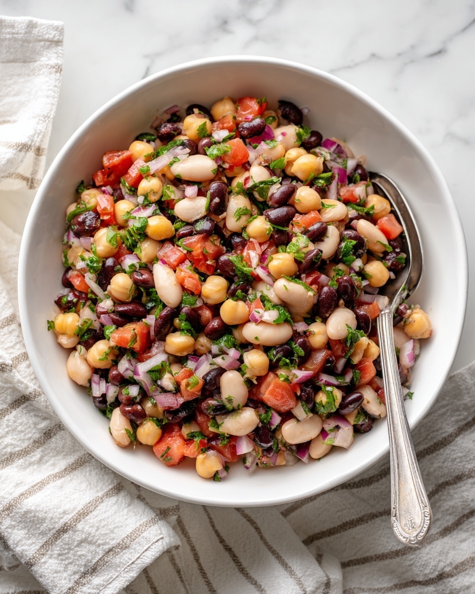 A stack of seven square crackers with a rough texture sits in the middle on a white marbled surface. On top of the stack, there is a mix of three layers of toppings: light beige chickpeas, dark red beans, and small pieces of red onion and bright red bell pepper. In the background, a large white bowl filled with more of the same bean and vegetable mix is slightly blurred, and loose chickpeas and one cracker are scattered on the surface. The scene is lit softly, emphasizing the textures and colors of the toppings photo taken with an iphone --ar 4:5 --v 7
