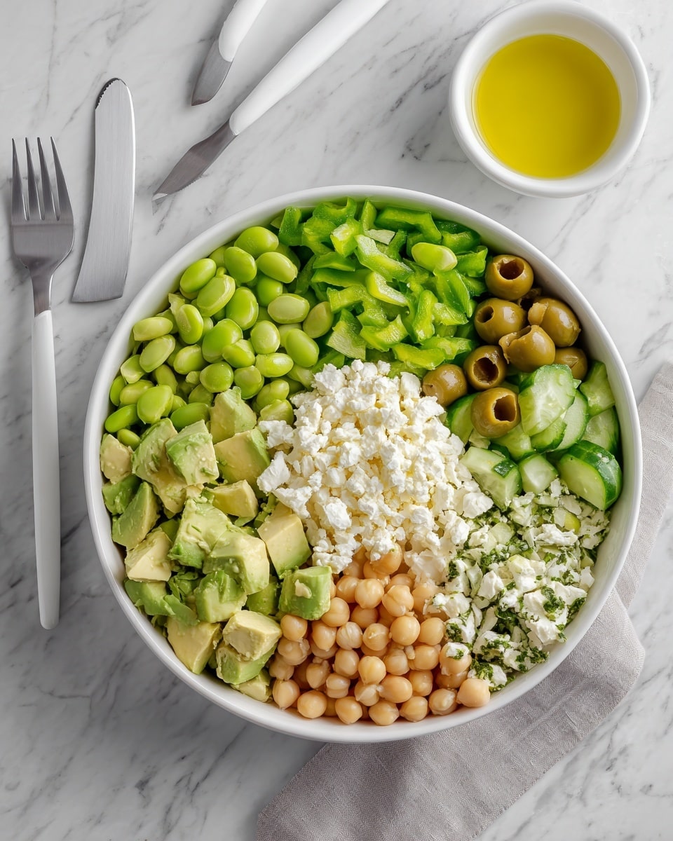 A round white plate holds a fresh salad made of three main layers: the bottom layer is chopped light green celery pieces, the middle layer has a mix of plump light beige chickpeas and bright green edamame beans scattered evenly, and the top layer consists of small white chunks of feta cheese and pale green artichoke hearts, all sprinkled with finely chopped dark green herbs. A white spoon rests on the right side of the plate, partially submerged in the salad. The whole scene is set on a white marbled texture surface. photo taken with an iphone --ar 4:5 --v 7