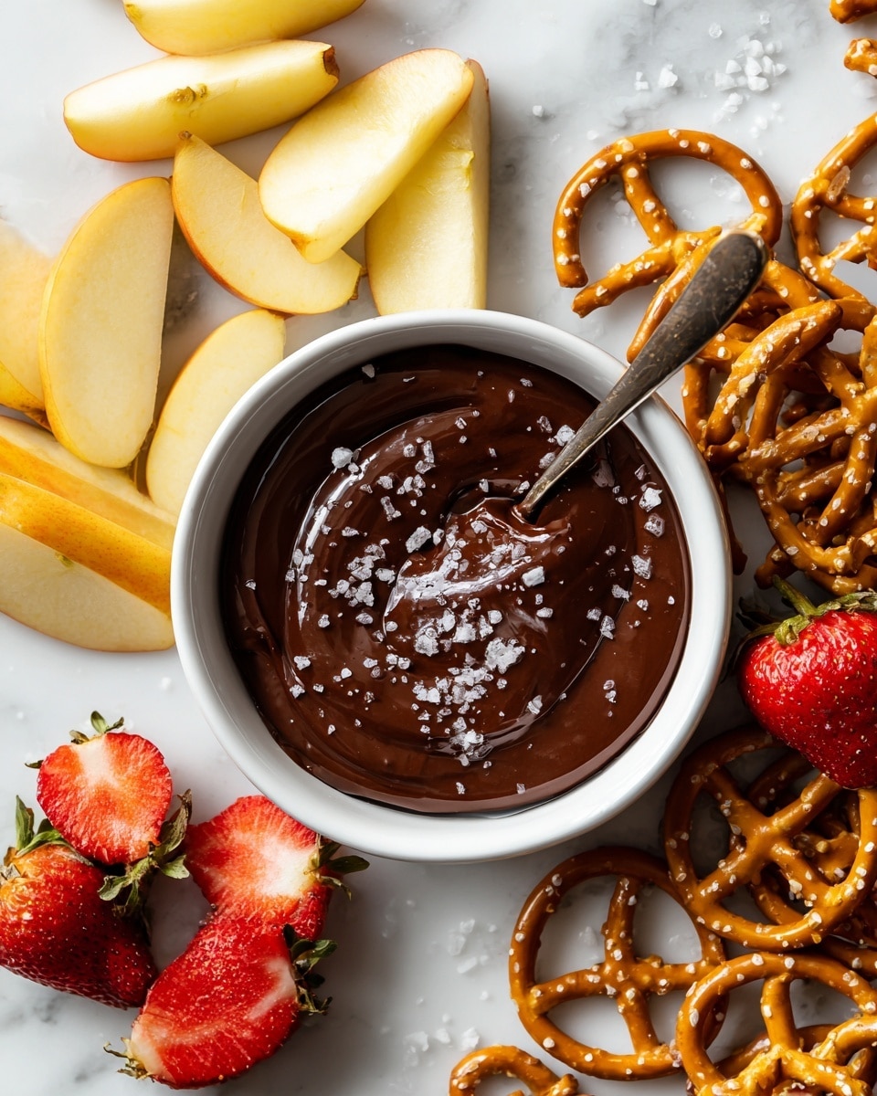 A white bowl filled with thick, dark brown chocolate dip, topped with coarse salt crystals. A woman's hand is dipping a bright red strawberry with a green stem into the rich chocolate dip. The bowl is placed on a wooden board, with part of a white marbled surface visible in the background and out-of-focus pretzels and more strawberries beside the bowl. photo taken with an iphone --ar 4:5 --v 7