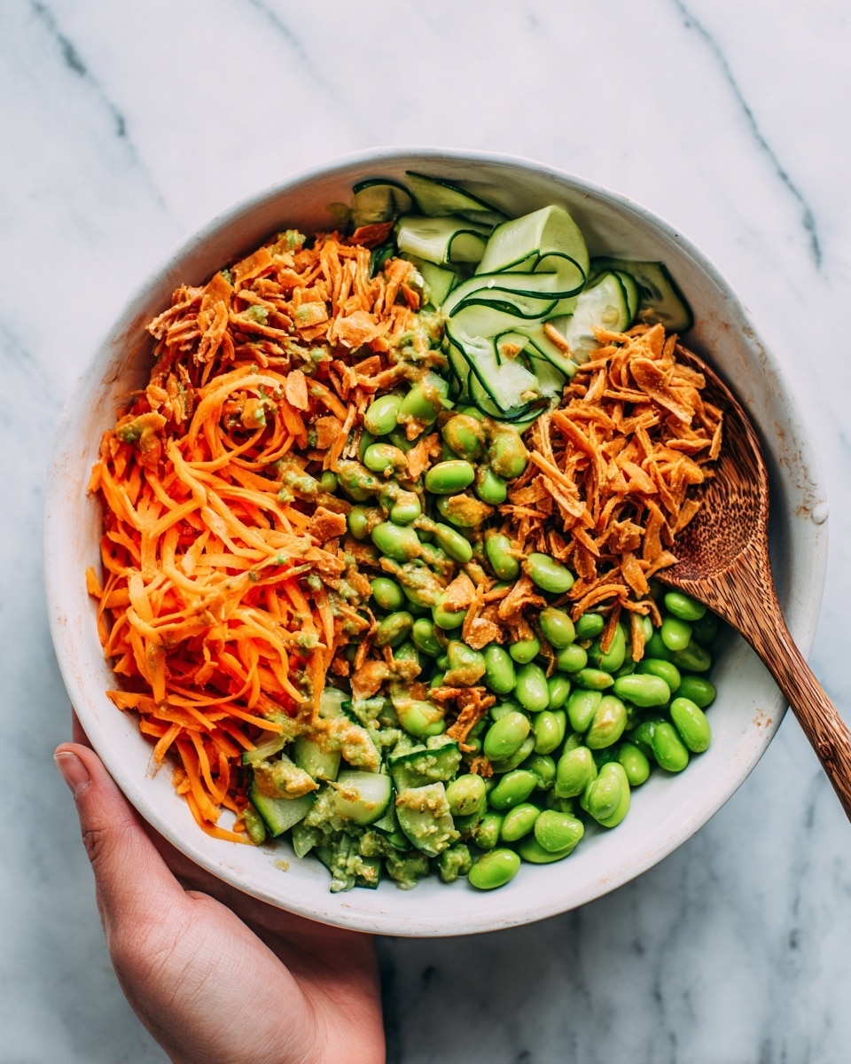 A white bowl filled with a colorful mix of food showing about three main layers: thin orange carrot strips and chunks of red bell pepper scattered throughout; bright green edamame beans and thin slices of cucumber evenly spread across the top and middle; and underneath, shredded brown textured pieces that could be cooked meat or plant-based protein. A wooden spoon rests inside the bowl on the right side, and a woman's hand holds the spoon, partially visible. The background surface is a white marbled texture. Photo taken with an iphone --ar 4:5 --v 7