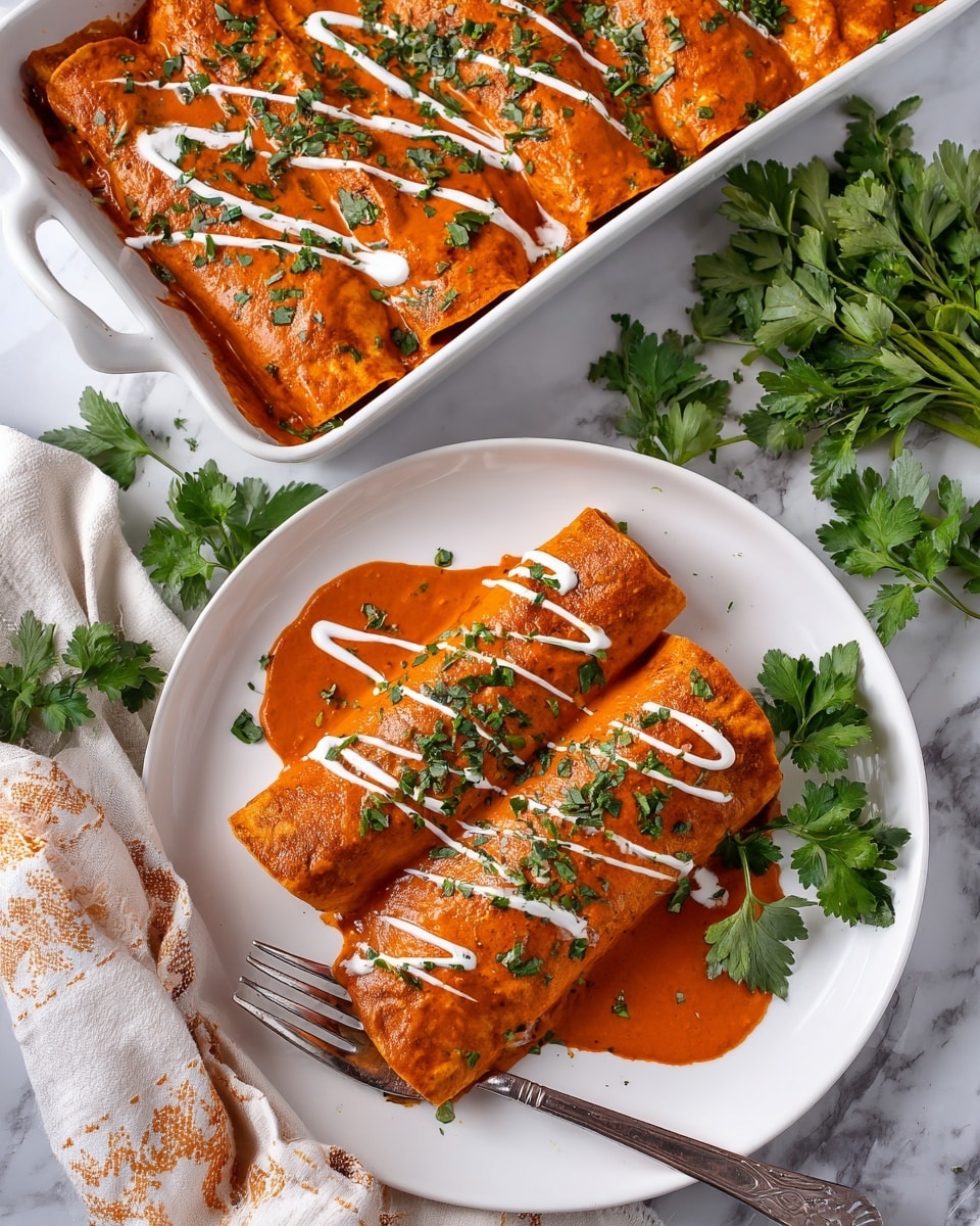 The image shows two rolled enchiladas placed on a white plate, covered evenly with an orange-red sauce that has a smooth texture, drizzled with thin lines of white cream sauce on top. Each enchilada is garnished with finely chopped green herbs scattered over the sauce, with a small bunch of fresh green parsley leaves placed at the base of the enchiladas. Next to the plate, there is a white rectangular baking dish filled with several more rolled enchiladas, fully covered in the same orange-red sauce and white cream drizzles, garnished with chopped green herbs. Surrounding the plate and baking dish are fresh sprigs of bright green parsley scattered across a white marbled surface. A metal fork rests on the plate with its tip partially under one enchilada. The photo taken with an iphone --ar 4:5 --v 7