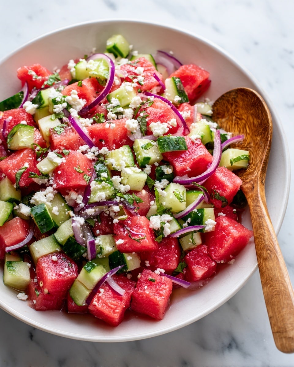 A white bowl with a brown rim holds a colorful salad made of chunky bright red watermelon cubes, thick green cucumber pieces with pale interiors, thin slivers of purple-red onion, and bits of white crumbled cheese sprinkled on top. The salad is mixed with small green herb bits scattered evenly. The bowl sits on a wooden utensil board with two wooden salad spoons to the side, and a cream and black checkered cloth napkin is partly under the bowl, all placed on a white marbled surface. photo taken with an iphone --ar 4:5 --v 7
