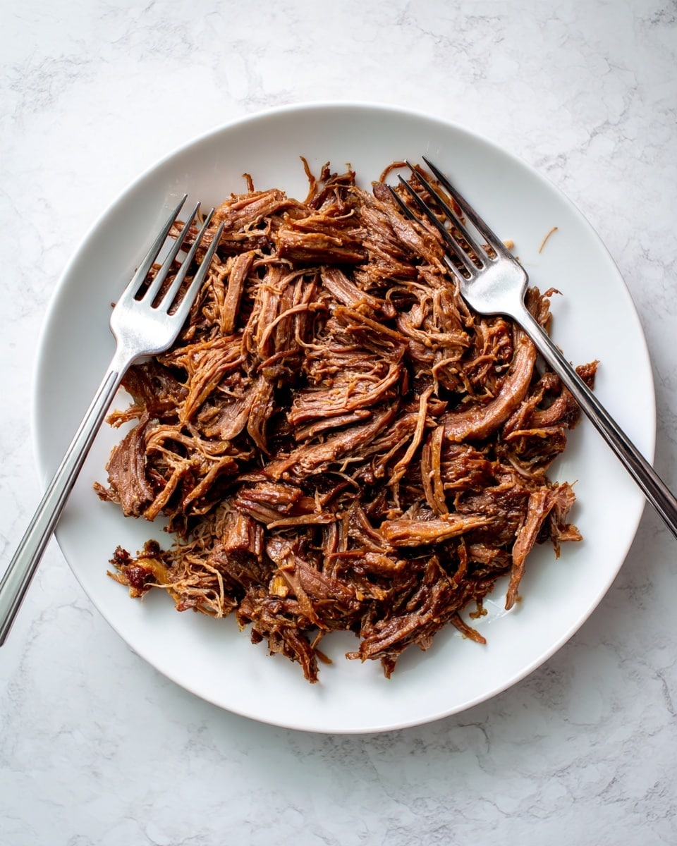A white plate filled with a single layer of brown shredded meat with visible fibrous texture, the meat appears tender and moist, covering the entire plate evenly. Two silver forks rest on the left side of the plate, one fork partially sticking into the meat. The plate sits on a white marbled textured surface, and the lighting is soft, highlighting the detailed strands of meat. photo taken with an iphone --ar 4:5 --v 7