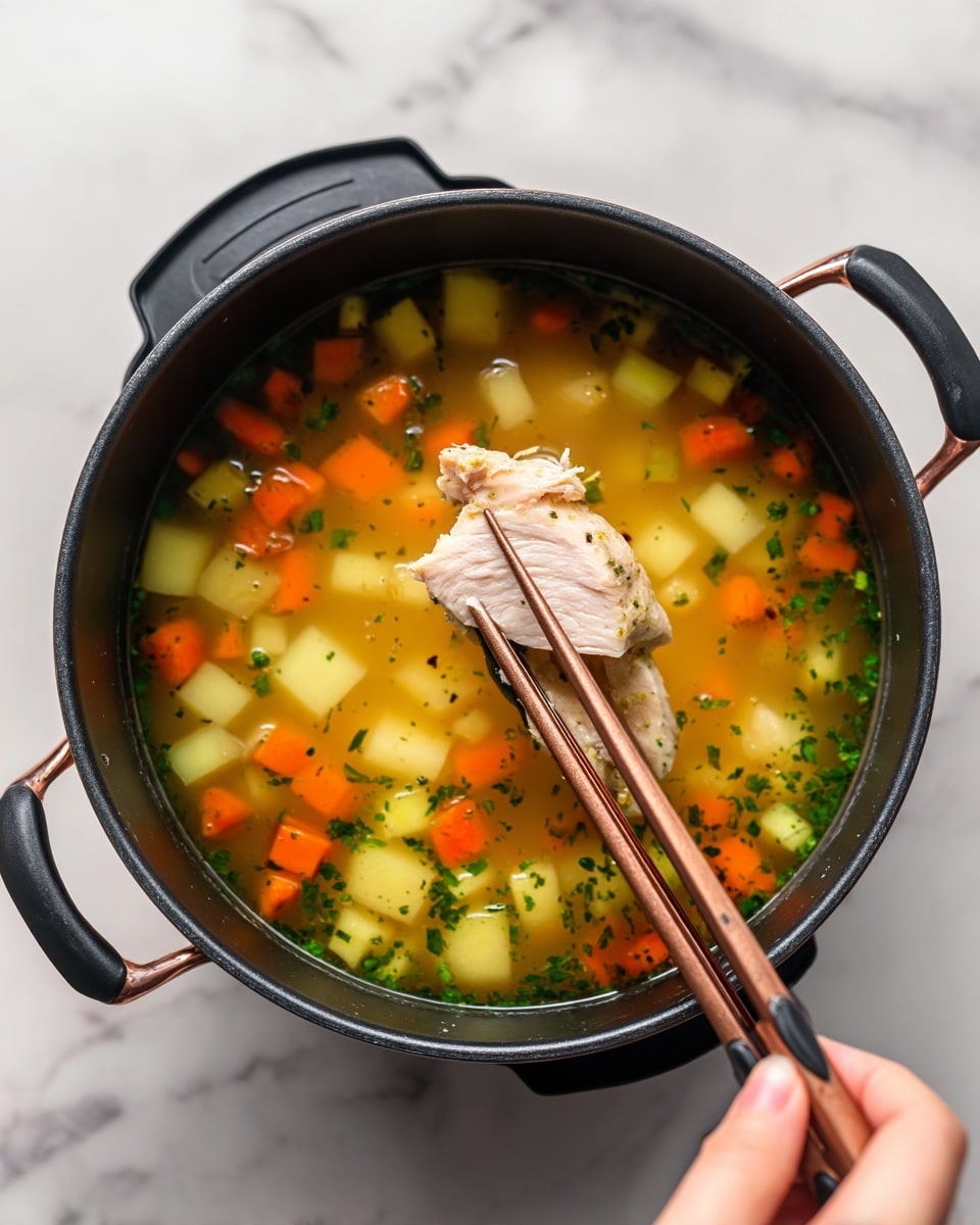 The image shows a black pot filled with a soup that has visible layers of diced orange carrots, light yellow potatoes, and green herbs floating in a clear broth. On top, a piece of cooked light beige chicken is being lifted by black tongs with copper handles, held by a woman's hand using wooden chopsticks for support. The scene is set on a white marbled background. The pot has a simple round shape and the colors of the soup ingredients contrast well with the dark pot. photo taken with an iphone --ar 4:5 --v 7