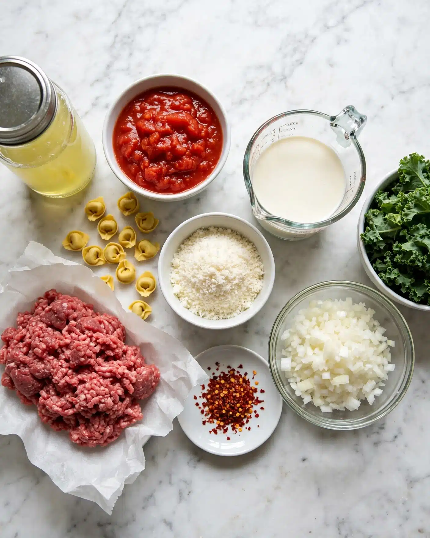 The image shows several cooking ingredients placed on a white marbled surface. On the left, there is a glass jar filled with a light yellow liquid. Next to it, a white bowl contains chunky red tomato sauce, and below it, raw ground meat lies on a piece of white parchment paper, showing a mix of red and pink colors. Above the meat are small yellow tortellini scattered across the surface. In the center, a small white bowl holds a grated white ingredient, next to a measuring cup filled with creamy white liquid. Below it, a white plate contains red chili flakes. To the right, there is a clear glass bowl filled with chopped white onions, and finally, a white bowl on the far right holds a pile of green leafy kale. Photo taken with an iphone --ar 4:5 --v 7