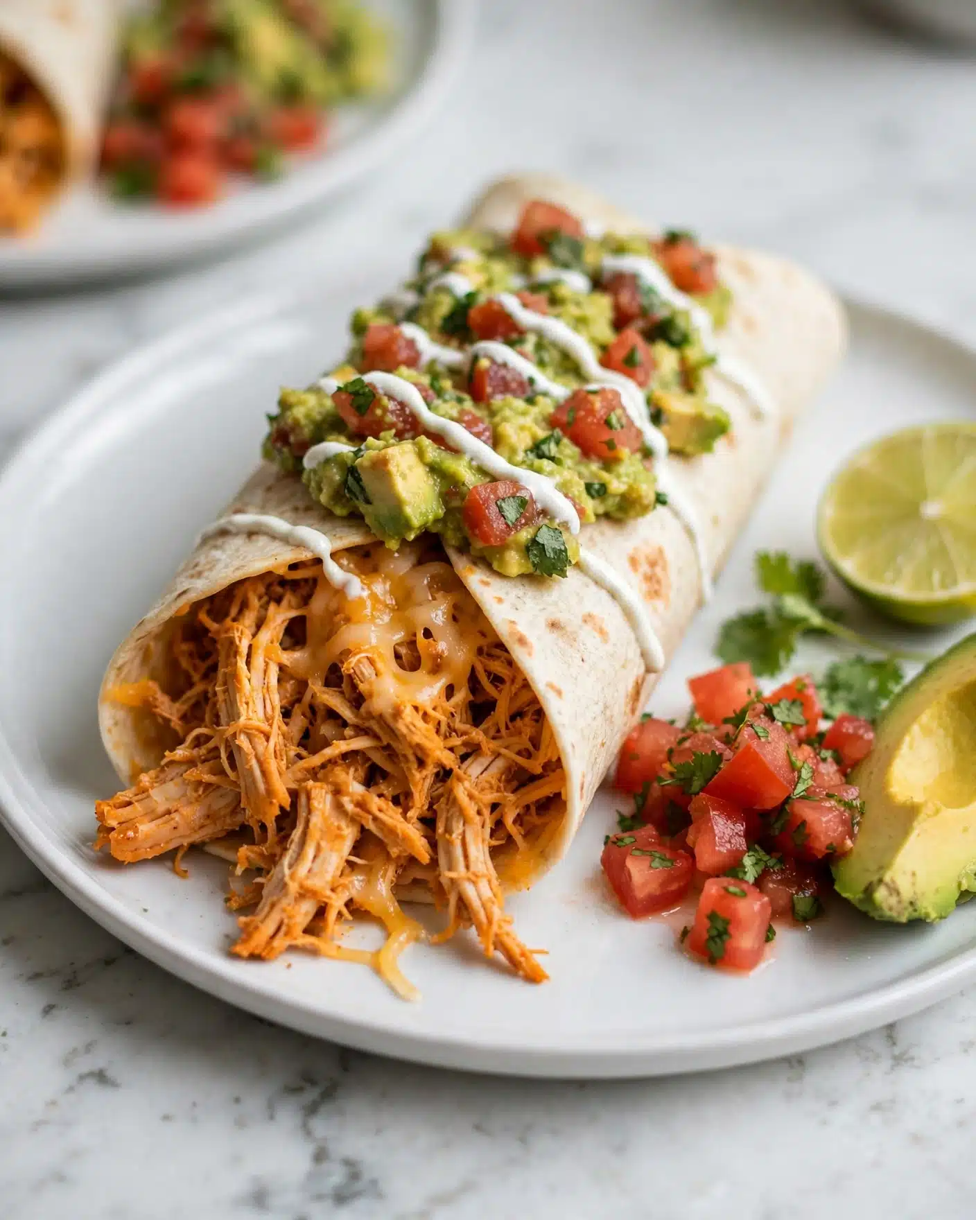 Baked or Pan-Fried Chicken Chimichangas Recipe 4 A golden-brown burrito sits in the center of a white plate with a slightly toasted texture. On top are three thin lines of white sauce and a fresh green guacamole layer with chunks of red tomato and green onion pieces. To the left of the burrito is a small pile of bright red and pink pico de gallo with bits of onion and green herbs. Behind that, there are two glossy, light green avocado slices, sprinkled with black pepper. To the right of the burrito, fresh bright green cilantro leaves spill onto the plate beside two lime slices with a vibrant green rind and a juicy pale green inside. The plate rests on a white marbled surface. Photo taken with an iphone --ar 4:5 --v 7